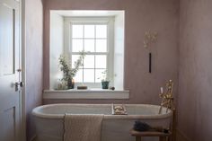 a bath tub sitting under a window next to a white sink in a room with pink walls