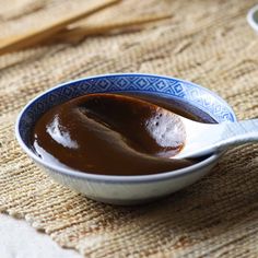 a spoon full of brown liquid on top of a table cloth next to two bowls