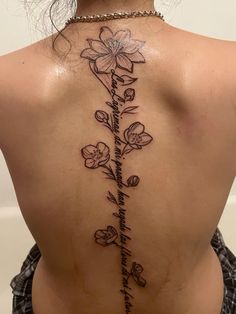 the back of a woman's neck with flowers and words tattooed on her lower back