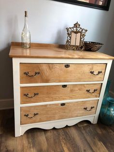 a white dresser with drawers and a bottle sitting on it's top, next to a blue vase