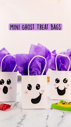 mini ghost treat bags on a table with purple tissue pom - poms around them