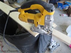 a yellow and black power tool sitting on top of a metal bucket next to a piece of wood