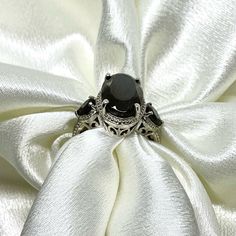 a black diamond ring sitting on top of a white satin fabric with an intricate design