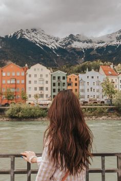 a woman is standing on a bridge looking at the water and mountains in the background