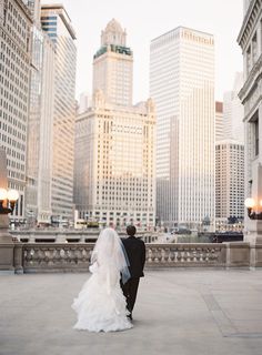 a bride and groom walking in front of the chicago skyline at their wedding day, with skyscrapers in the background