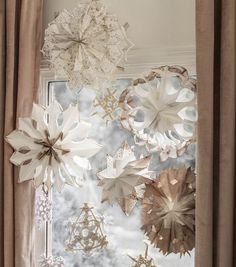 paper snowflakes hanging from the ceiling in front of a window with drapes