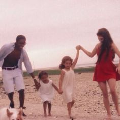 a man and two girls are holding hands with a dog on the beach next to them