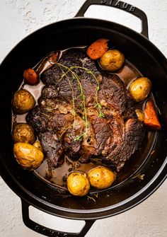 a pot filled with meat and potatoes on top of a table next to a wall