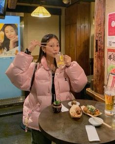 a woman sitting at a table drinking from a glass in front of her face with food on the table