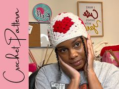 a woman wearing a crocheted hat with red flowers on it and holding her hands to her face