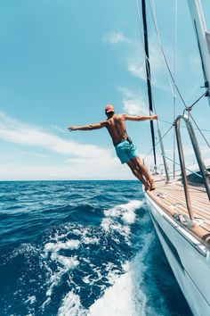 a man jumping off the side of a sailboat into the ocean with his arms outstretched