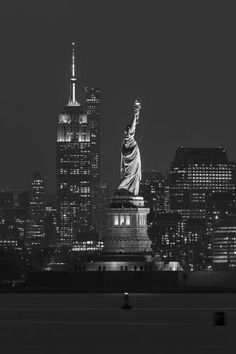 the statue of liberty in new york city at night with empire building and skyscrapers behind it