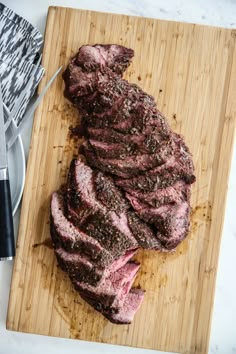 a steak on a cutting board next to a knife and fork with another meat in the background