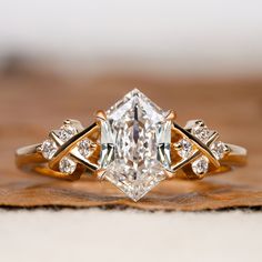 an engagement ring with a large diamond surrounded by smaller diamonds on top of a piece of wood