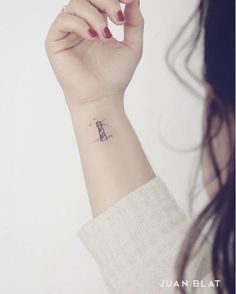 a woman's wrist with a small lighthouse tattoo on the left side of her arm