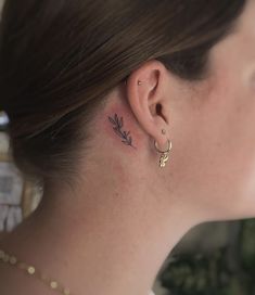 a woman with a small tattoo on her left ear and behind her ear is a plant