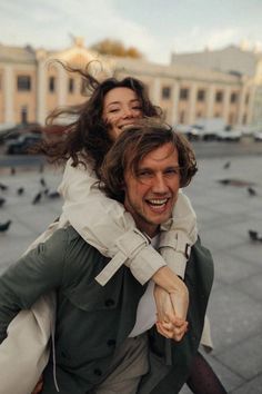 a man carrying a woman on his back in the middle of a street with pigeons flying around