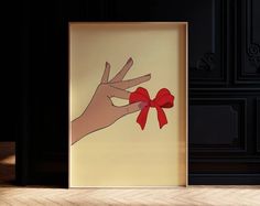 a hand holding a red bow in front of a framed photo on the floor next to a black wall