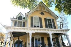 a yellow house with black shutters on the front door and windows, has a wrought iron fence around it