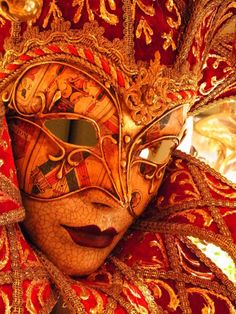 a woman wearing a red and gold mask on top of her head with an ornate pattern