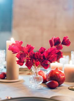 red flowers in a vase sitting on top of a table next to candles and plates