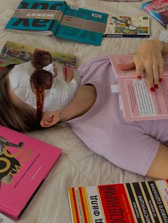 a woman laying on top of a bed with lots of books next to her face