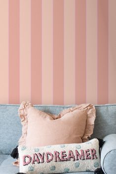 a blue couch with a pink striped wall behind it and a decorative pillow on the back