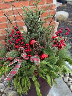 a potted plant with pine cones, berries and greenery in it is sitting on some rocks