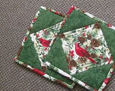 three quilted placemats sitting on top of each other with pine cones and cardinals