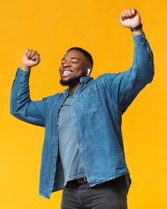 a man with his arms in the air, smiling and raising his fist up while standing against a yellow background