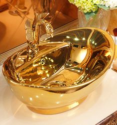 a gold bathroom sink sitting on top of a counter next to a vase with flowers