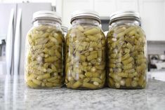 three jars filled with green beans sitting on top of a counter