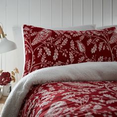 a bed with red and white comforter next to a lamp on the side table