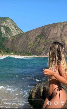 a woman standing on top of a rocky beach next to the ocean with mountains in the background