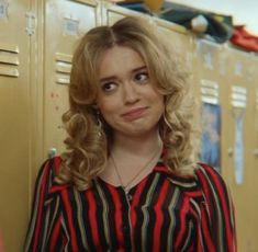 a woman standing in front of lockers wearing a red and black striped shirt with her hands on her hips