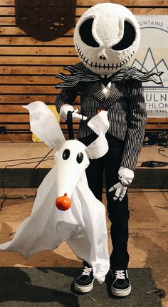 a person in a costume standing next to a white dog wearing a jack skellingy hat