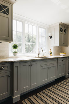 a kitchen with gray cabinets and an area rug in front of the window that has a potted plant on it