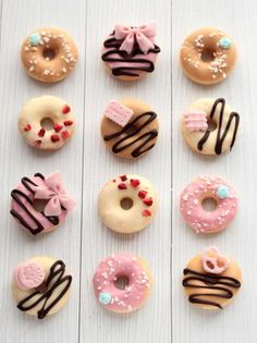 twelve donuts decorated with different types of icing and sprinkles on white wood