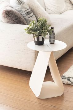 a white table sitting on top of a wooden floor next to a couch and potted plant