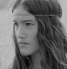 a woman with long hair wearing a chain around her head and looking off into the distance