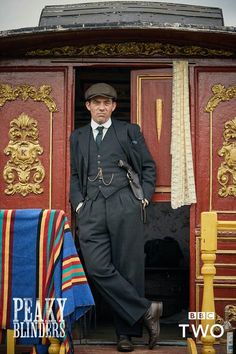 a man standing in the doorway of a train car wearing a suit and hat with his hands on his hips