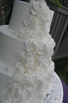 a three tiered white wedding cake with flowers on the top and bottom, sitting on a purple table cloth