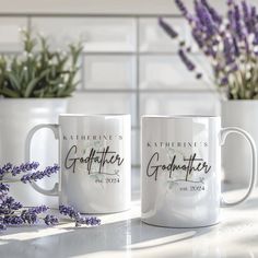 two white coffee mugs sitting on top of a counter next to lavender flowers and potted plants