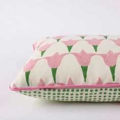 a pink and green pillow with white flowers on the front, sitting on a white surface