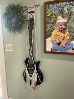 a guitar hanging on the wall next to a framed photo and a small planter