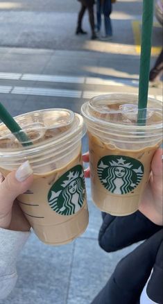 two people holding up starbucks drinks on the street