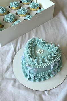 a heart shaped cake sitting on top of a table next to cupcakes