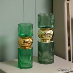 two green glass vases sitting next to each other on a white counter top in front of a blue wall