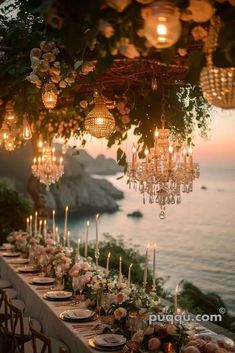 an outdoor dining table with candles and flowers on it, overlooking the ocean at sunset