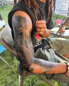 a man with dreadlocks is sitting in a chair and has tattoos on his arm